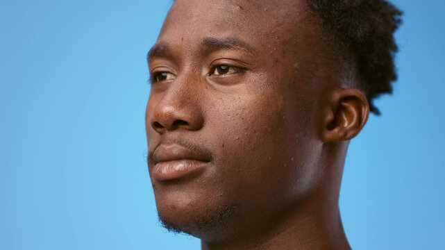 A young African American man gazes thoughtfully against a bright blue background, showcasing his calm demeanor. The lighting emphasizes his features, creating a striking contrast.
