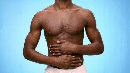 A young shirtless African American man touching his tummy, suffering from stomach ache. The bright blue background