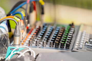 professional audio mixing console with colorful knobs, sliders, and connected xlr cables at outdoor...