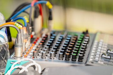 professional audio mixing console with colorful knobs, sliders, and connected xlr cables at outdoor...