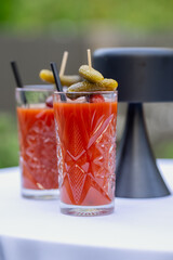 two bloody mary cocktails in crystal glasses with pickles and olives on skewers, served on white...