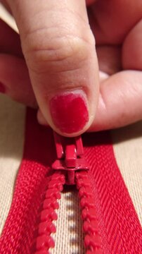 A macro shot showcasing a hand pulling a red zipper on beige fabric. The tailor is opening a zipper.