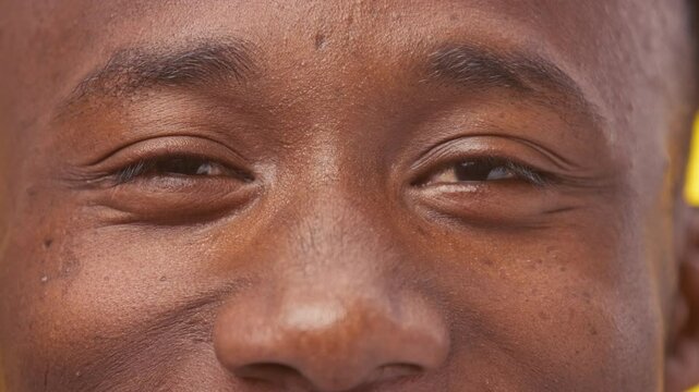 A young man of African American descent is smiling warmly, showcasing his distinctive features. The warm, natural light highlights his joyful expression against a soft background.