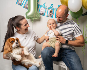 Joyful young parents holding their smiling one-year-old son and Cavalier King Charles Spaniel dog....