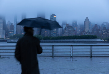 Person holding umbrella at dusk along the city waterfront