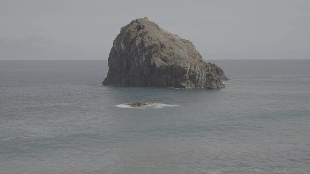 Lonely basalt islet rises from jewel tone Atlantic beside Madeira stone shore (SLOG3)