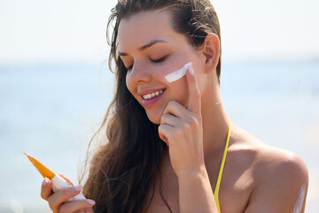 Beautiful woman enjoying a sunny day at the beach while applying sunscreen to protect her skin from...