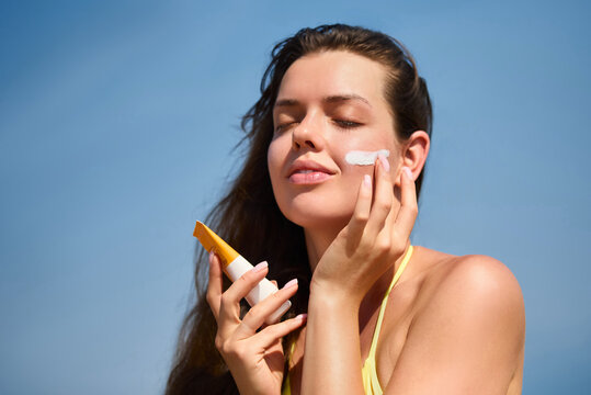 Beautiful woman applying sunscreen on her face while enjoying a sunny day outdoors, promoting skincare and sun protection for healthy skin. Skincare concept