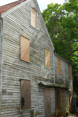 Abandoned old Wooden House with Boarded Windows Surrounded by Greenery. Weathered wooden house with boarded-up windows and signs of neglect, situated in a lush green environment. The image conveys aba