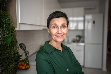 Joyful mature woman smiling happily looking at camera at home, natural self. Self acceptance, authenticity, mature beauty, inner peace, comfortable solitude, graceful aging, personal contentment