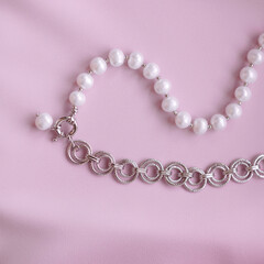 Close-up of elegant bracelet with white pearls and textured silver links on pink satin fabric. Jewelry detail for fashion, femininity, elegance, and gift concepts. Luxury and beauty theme.
