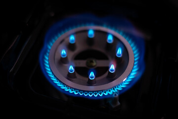 Close-up of a lit gas burner with blue flames in a dark setting, showing energy, heat, and kitchen technology with a focus on fire safety and home cooking
