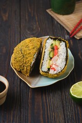 Fried sushi burgers in breading with crab sticks, cucumber and avocado filling on leaf-shaped plate on dark wooden background. Asian cuisine.