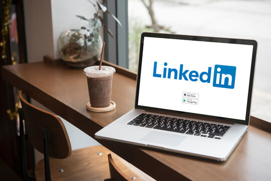 Laptop showing linkedin website on wooden table with iced coffee