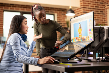 In creative workspace where diverse women are selecting images for color grading for an upcoming commercial project. Asian and african american designers focusing on retouching photographs in studio.