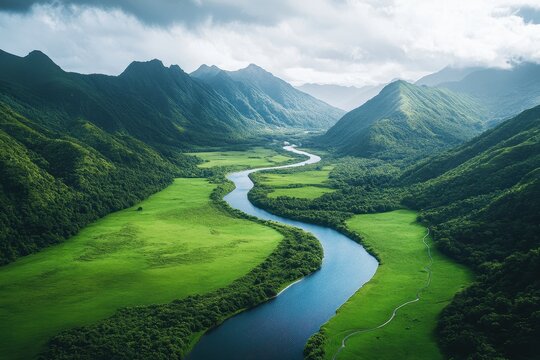 Aerial view of winding river flowing through lush green hills and mountains with fog lingering in the valleys in a tranquil landscape - Powered by Adobe