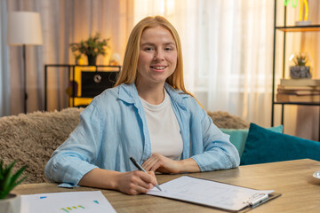 Young woman analyzes contract document at home, looking at page and verifying crucial points with...