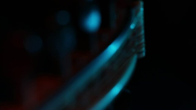 A dramatic close-up rack focus reveals the wooden bridge and strings of a cello. Moody blue and orange light creates a cinematic atmosphere against a dark background.