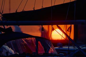 A yacht club at sunset, the big sun in the background, the sail is mounted on the mainsail,...