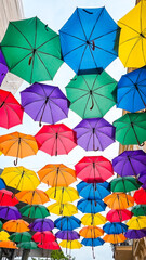  Bright red, yellow, blue, green, and purple umbrellas form a vivid overhead pattern, suspended in the air and glowing against the daylight sky&mdash;a joyful splash of color and creativity.