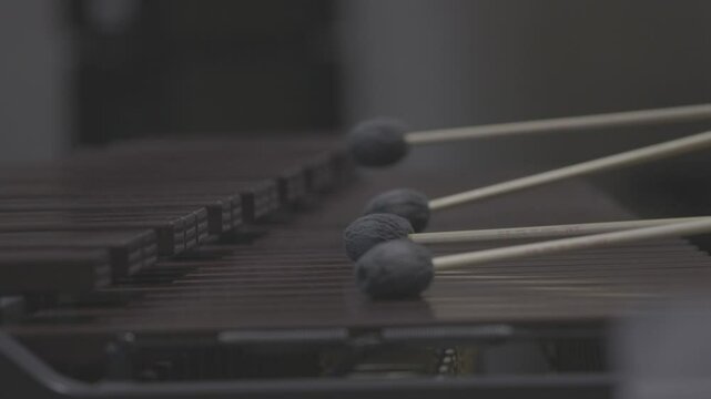 A close-up, low-angle shot of a musician passionately playing a marimba or vibraphone with mallets in a dark, atmospheric setting. Ungraded LOG footage for color grading.