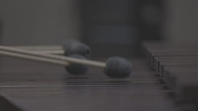 A close-up, low-angle shot of a musician passionately playing a marimba or vibraphone with mallets in a dark, atmospheric setting. Ungraded LOG footage for color grading.