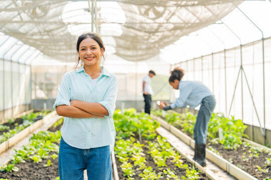 Happy teenage boy and girl growing and caring organic vegetables in greenhouse garden. Young farmer teamwork learning agriculture recording data on digital tablet analysis plant growth in organic farm