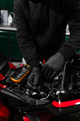 Mechanic testing battery with multimeter. Motorcycle battery is tested using digital multimeter to check voltage and health. Digital multimeter reads motorcycle battery voltage during inspection.