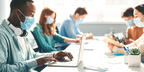 New Reality, Lifestyle And People Concept. Group of diverse international students or employees wearing protective medical masks and using laptop computers, studying and working at campus library