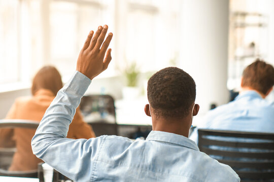 Education Concept. Rear back view portrait of african american guy student raising hand for answer or asking question, sitting at desk wearing surgical face mask at lecture in university or college