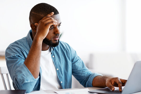 Modern Entrepreneurship. Young African American Businessman Working Online With Laptop At Home Office, Millennial Black Man Sitting At Desk, Looking At Computer Screen, Having Remote Job, Free Space - Powered by Adobe