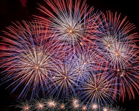 Abstract patterns of red, white, and blue fireworks filling the night sky.