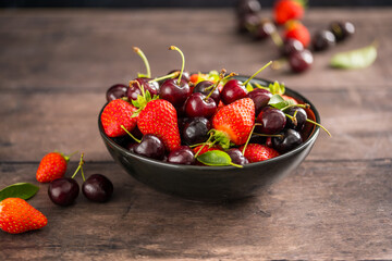 Fresh cherries and strawberries in a black plate, dark wooden background, fresh fruits