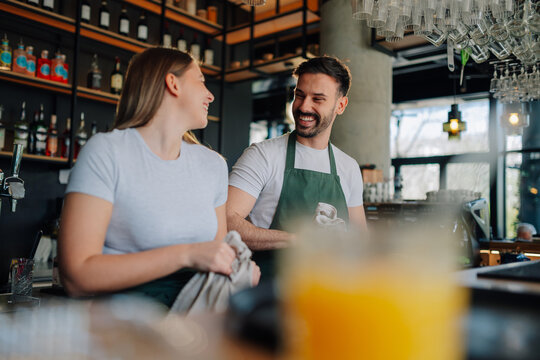Two smiling baristas chatting happily during work in modern cafe