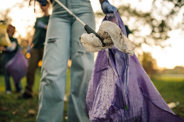 Volunteer picking up trash with trash grabber tool in public park