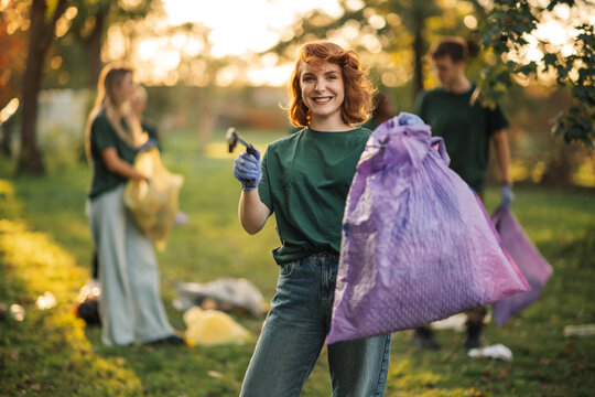 Young woman volunteer holding trash bag and smiling at camera in park