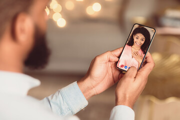 Long Distance Relationship. Back over the shoulder view of black man having online virtual date with his surprised girlfriend, holding and using smartphone app for videochat. Remote Dating
