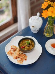 Thai food. Local Name is Kang Kiew Wan is Thai chicken vintage wooden, nearby is a pot of tea and teacup. Green Curry served with Roti flour by the window. Soft window light.