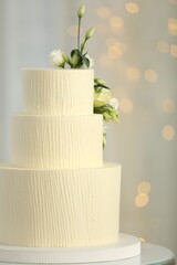 Delicious wedding cake with floral decor on table against blurred background, bokeh effect