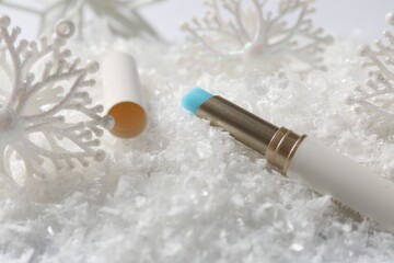 Moisturizing lip balm and Christmas decor on artificial snow, closeup. Winter care