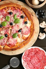 Tasty pizza, ingredients and cutter on black wooden table, flat lay