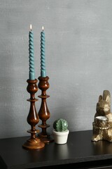 Elegant candlesticks with burning candles and other decor on black wooden table near grey wall
