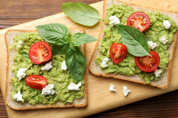 Delicious sandwiches with avocado, tomatoes, basil and cheese on wooden table, top view