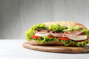 Tasty baguette sandwich with ham and vegetables on light grey table, closeup