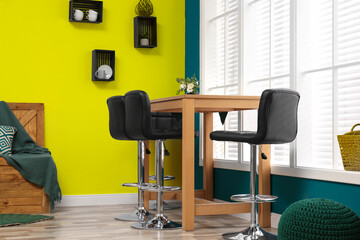 Wooden dining table and chairs in room. Interior design with yellow and teal walls