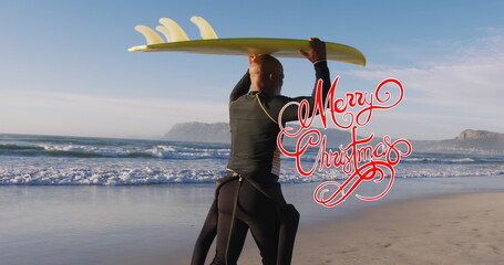 Mature male surfer raising yellow surfboard overhead on sandy shoreline, with black wetsuit