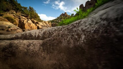 Rocky landscape featuring boulders, vegetation, and clear sky in mountainous terrain with textured rock surface in foreground