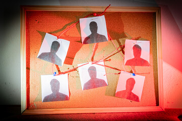 Criminal investigation board with suspect photos connected by red thread on cork background