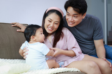 Parents and little baby are sitting on the sofa at home. They are happy. Family concept. Good development of your beloved child starts with parents.