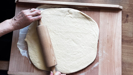 Top view of woman's hands rolling dough on wooden table with wooden rolling pin. Homemade baking,...